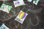 Kolorowe rysunki na chodniku, w centrum rysunek tęczowego balonu, który unosi się nad wyklejonym ze sznurków gniazdem; w gnieździe są malutkie rysunki kotów - każdy naklejony na nie, narysowany na osobnym urywku papieru.