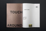 Zdjęcie; otwarty katalog wystawy; karta po lewej w kolorze brązowym i wytłoczonym nieregularnym znakiem; na tym napis: TOUCH AROUND; karta po prawej biała - ma geometryczne znaki oraz niewielkie zdjęcie wychudzonej krow